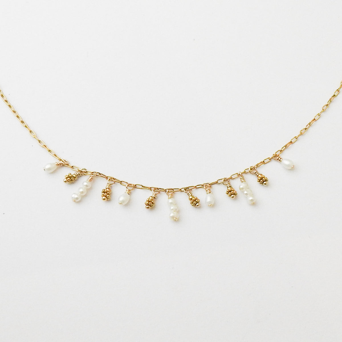 A delicate gold chain necklace featuring small dangling pearl beads and textured gold bead accents, displayed against a clean white background.