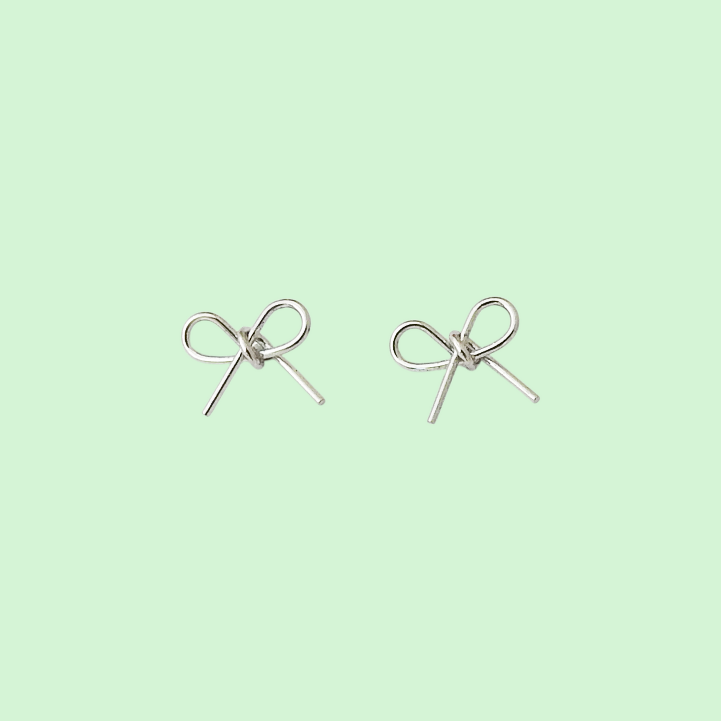A pair of silver bow stud earrings on a solid pale mint green background.