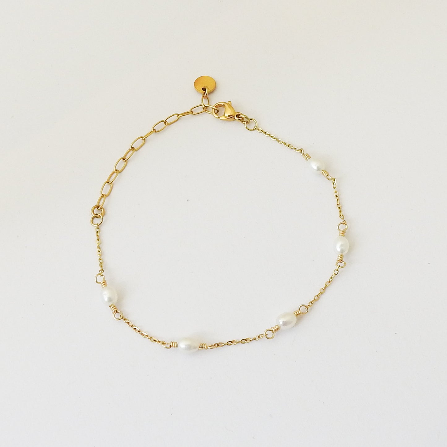 A delicate gold chain bracelet with small white pearl beads spaced along the chain, displayed on a clean white background.