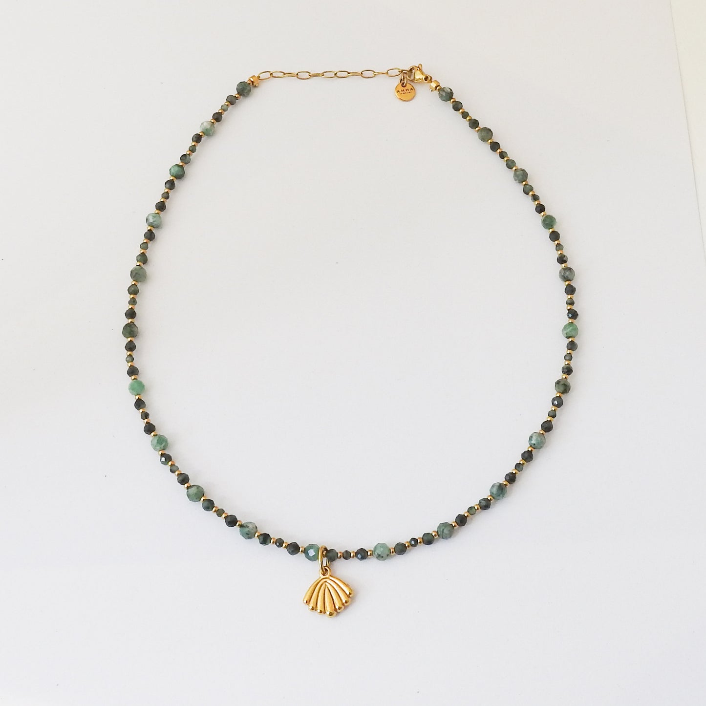 A beaded necklace featuring small green and dark green beads with a gold-tone clasp and a gold-tone shell-shaped pendant, displayed on a clean white background.