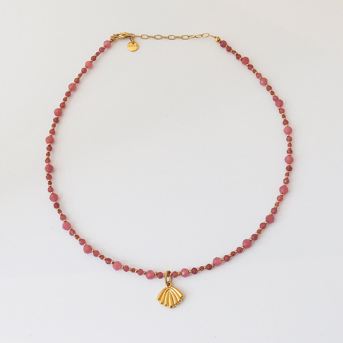 A beaded necklace featuring faceted pinkish-red beads and a gold shell pendant, displayed on a clean white background.