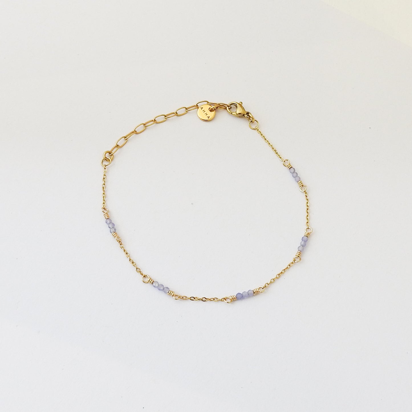 A delicate gold chain bracelet with small light purple beads spaced along the chain, displayed on a clean white background.