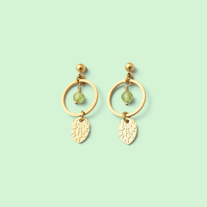 A pair of gold dangle earrings with circular hoops, small bead accents, and leaf-shaped charms, shown on a solid pale mint green background.