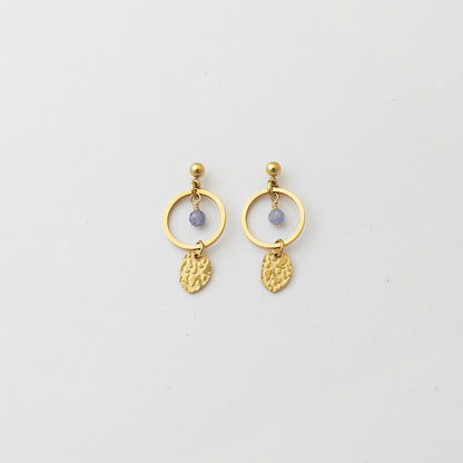 A pair of gold drop earrings featuring a circular ring, a small round purple bead, and a textured gold leaf-shaped dangle, shown on a plain light gray background.