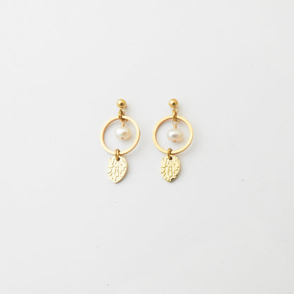 A pair of gold dangle earrings featuring a small white pearl, a gold ring, and a textured leaf-shaped charm, displayed on a clean white background.