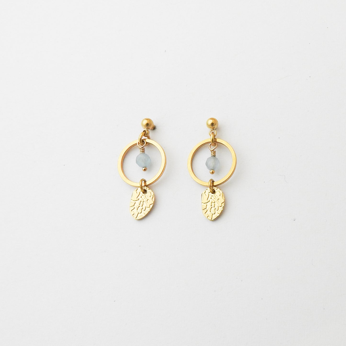 A pair of gold dangle earrings with circular hoops, small light blue beads, and textured leaf charms, displayed on a clean white background.
