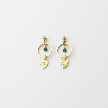 A pair of gold dangle earrings with a small green bead and a textured gold leaf charm, displayed on a clean white background.