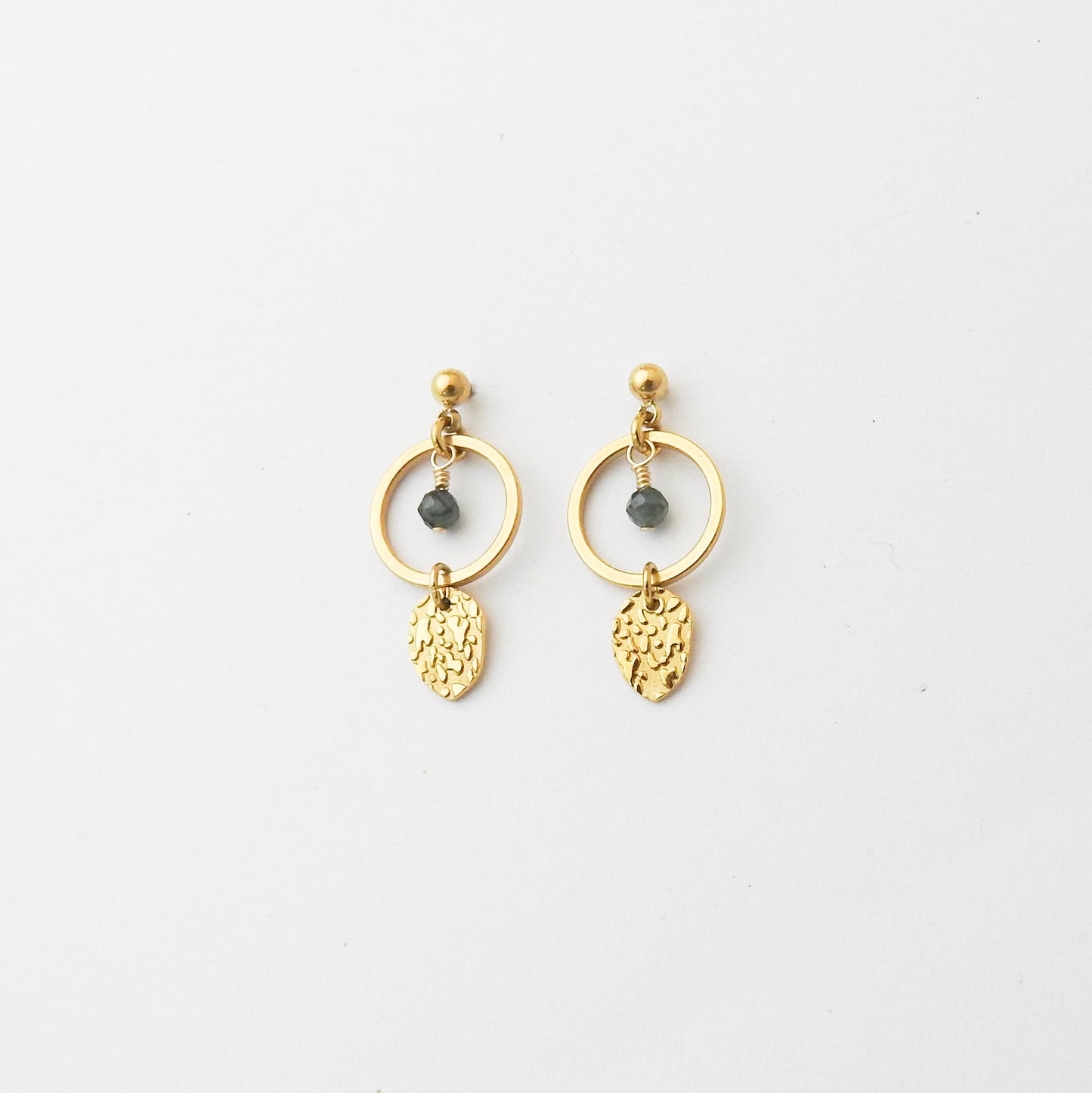 A pair of gold dangle earrings with circular hoops, small dark gray bead accents, and textured leaf-shaped charms, displayed on a clean white background.
