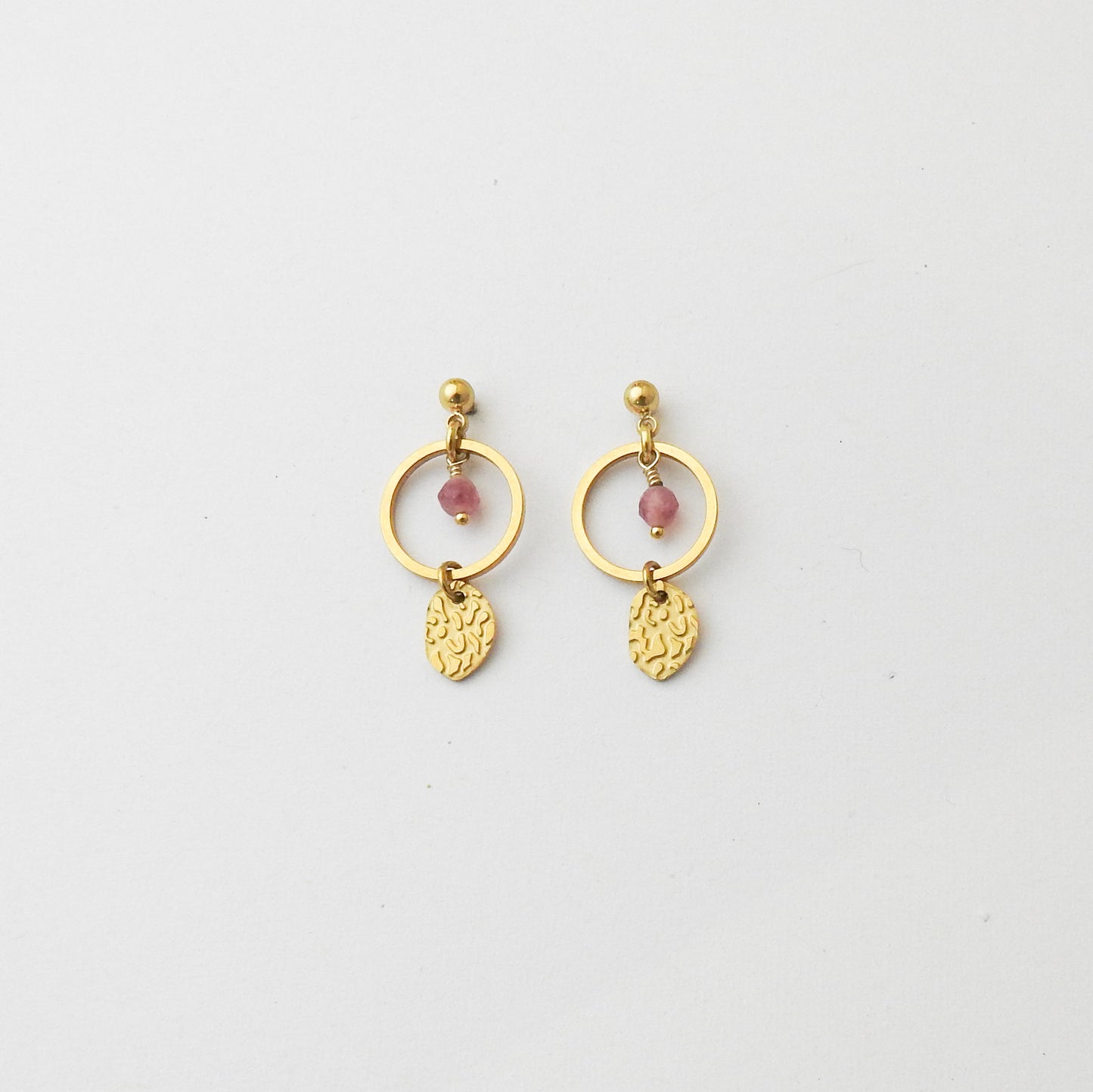 A pair of gold dangle earrings with circular hoops, small pink bead accents, and textured leaf-shaped charms, displayed on a clean white background.