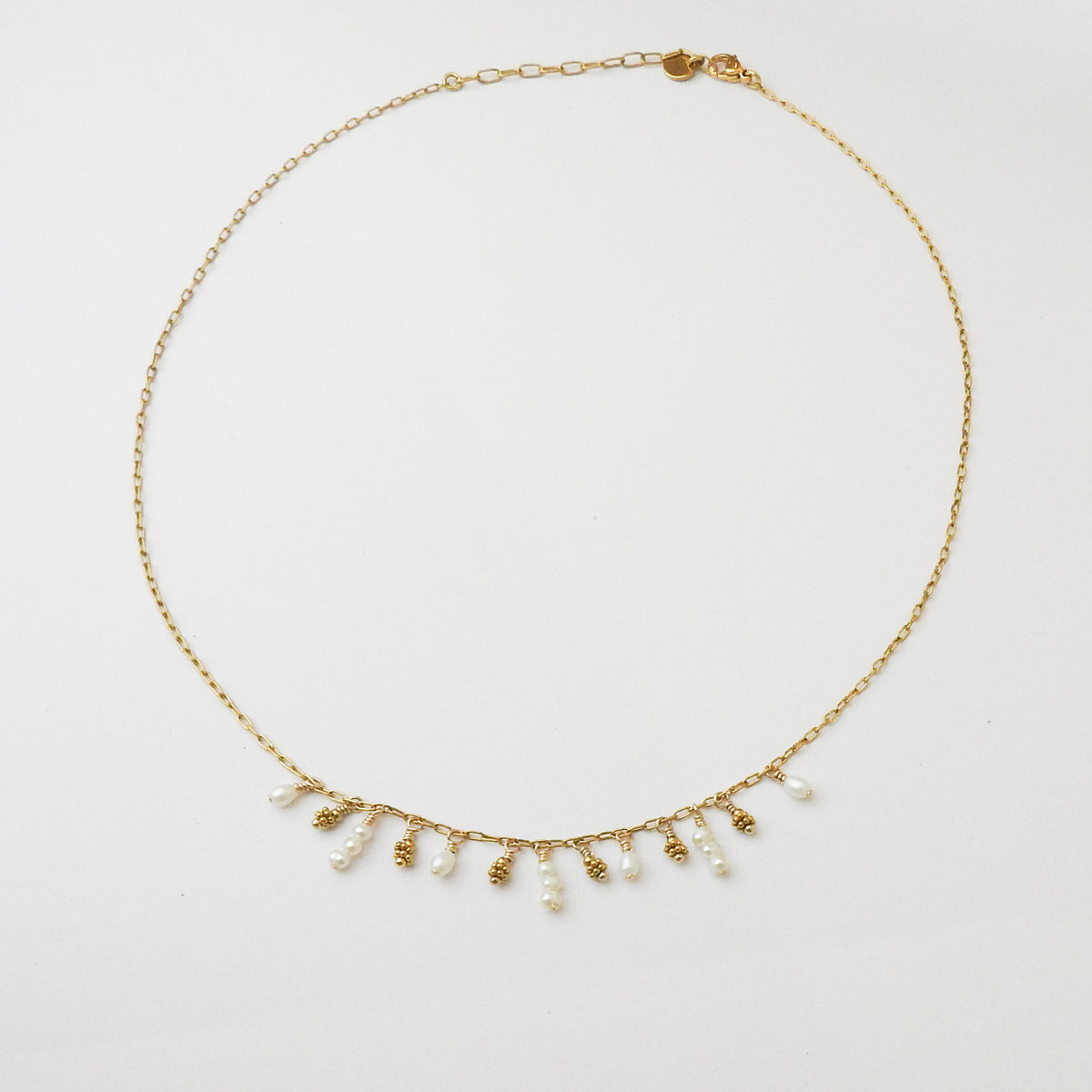 A delicate gold chain necklace featuring a fringe of small white freshwater pearls and textured gold bead drops, displayed on a clean white background.