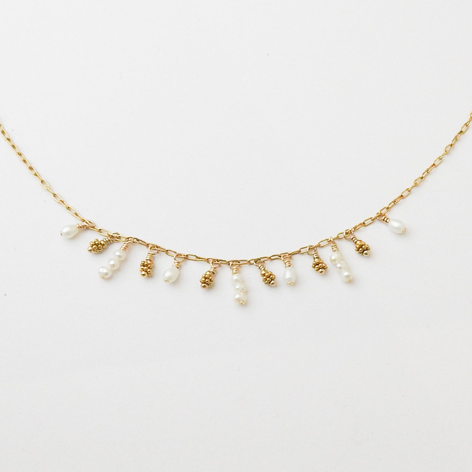 A delicate gold chain necklace featuring small dangling pearl beads and textured gold bead accents, displayed against a clean white background.