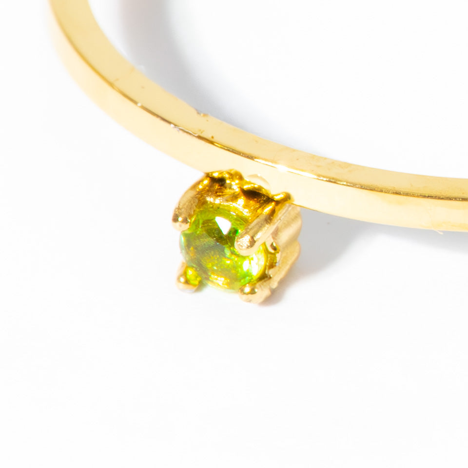 A close-up of a gold ring featuring a round-cut green gemstone in a prong setting, shown against a plain white background.