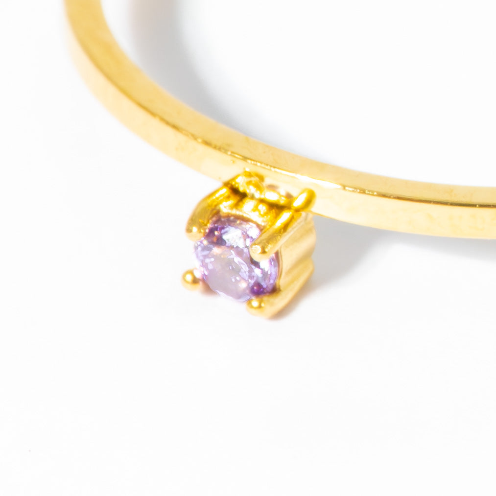A close-up of a gold ring featuring a round-cut light purple gemstone in a prong setting, shown against a plain white background.