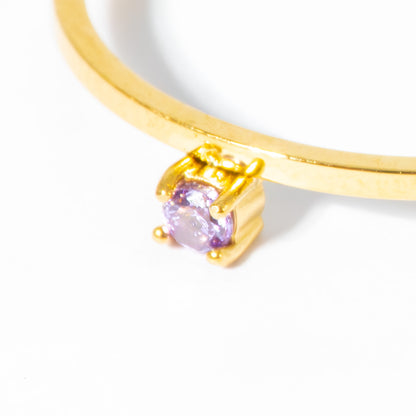 A close-up of a gold ring featuring a round-cut light purple gemstone in a prong setting, shown against a plain white background.