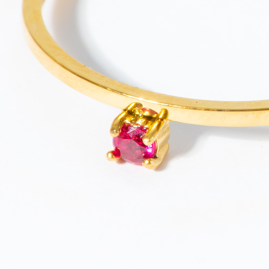 A close-up of a gold ring with a single round-cut pink gemstone in a prong setting, shown against a plain white background.