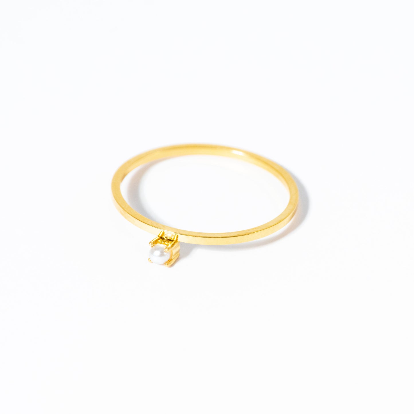 A delicate gold ring featuring a small, clear, bezel-set round gemstone, photographed on a seamless white background.