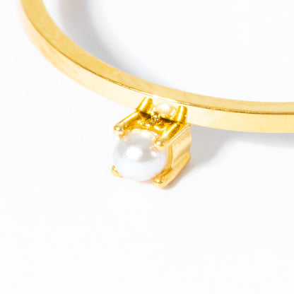 A close-up of a gold bangle bracelet featuring a small gold chair holding a white pearl, set against a clean white background.