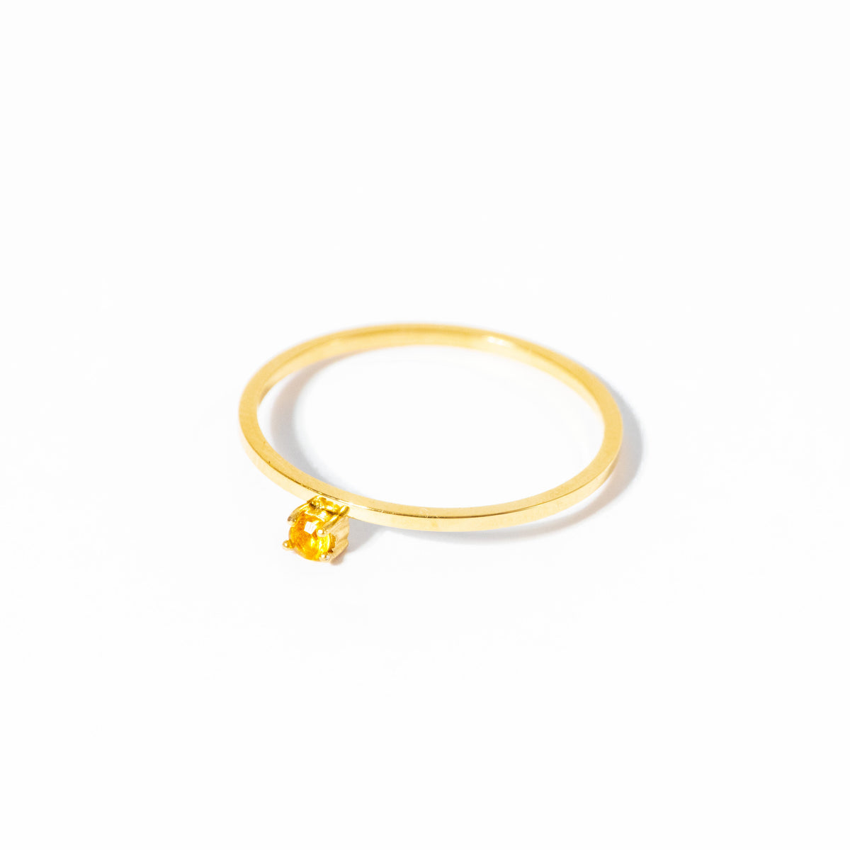 A delicate gold ring featuring a small, square-cut yellow gemstone in a prong setting, photographed on a seamless white background.