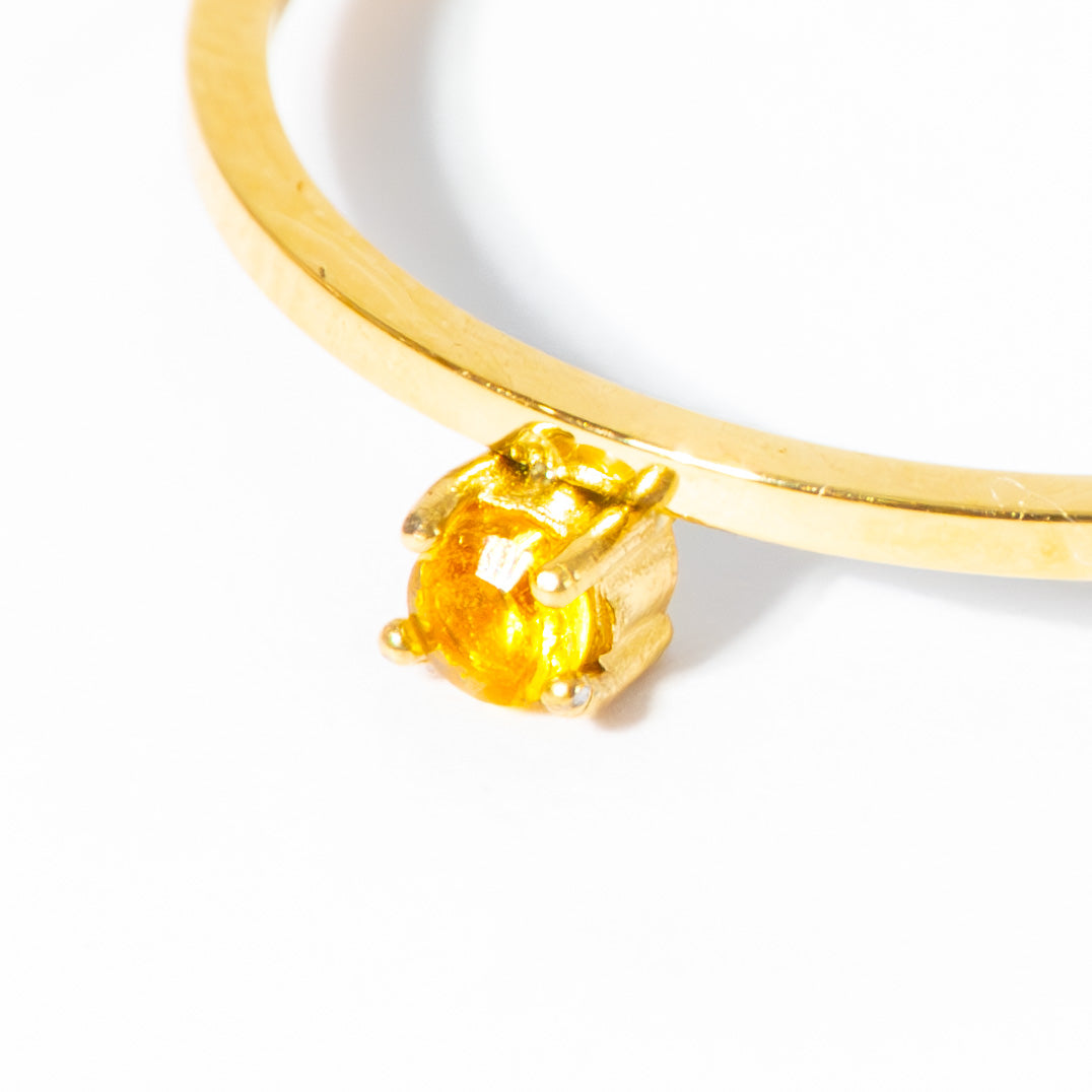 A close-up of a gold ring with a round yellow gemstone in a prong setting, photographed on a plain white background.