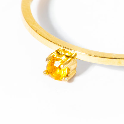 A close-up of a gold ring with a round yellow gemstone in a prong setting, photographed on a plain white background.