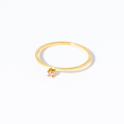 A delicate gold ring featuring a small, clear teardrop-cut gemstone in a gold setting, photographed on a seamless white background.
