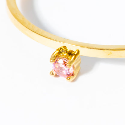 A close-up of a gold ring featuring a round pink gemstone in a prong setting, shown against a plain white background.