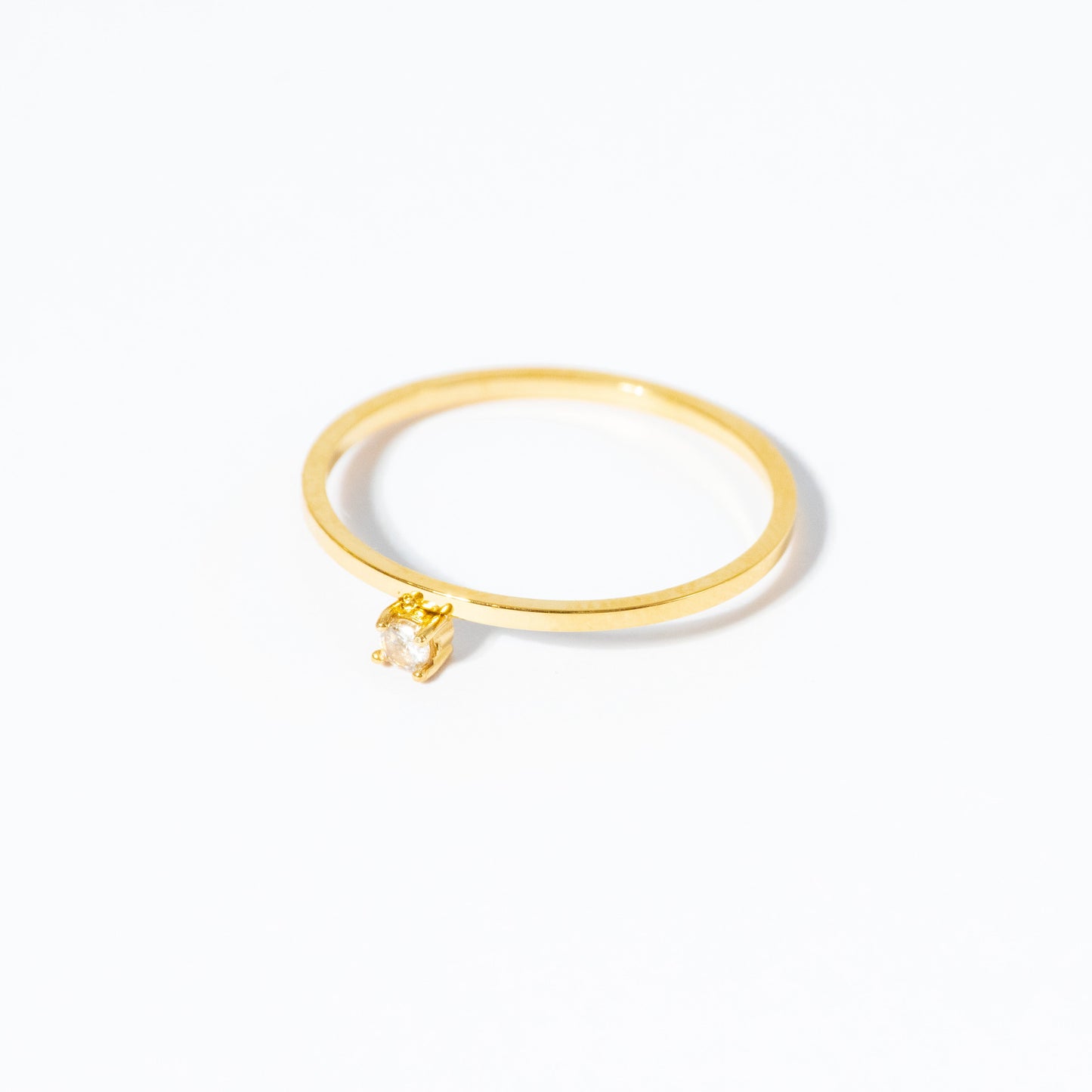 A delicate gold ring with a small, abstract geometric dangling charm, photographed on a seamless white background.