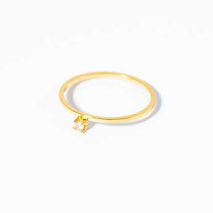 A delicate gold ring with a small, abstract geometric dangling charm, photographed on a seamless white background.