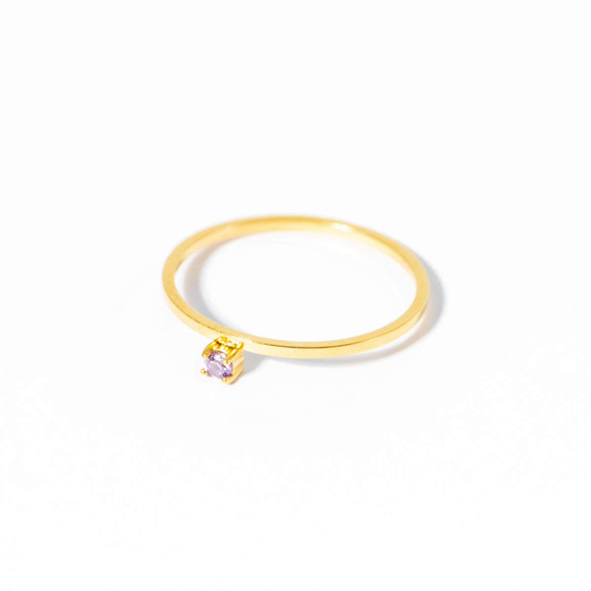 A minimalist gold ring with a single small square-cut light purple gemstone in a bezel setting, photographed on a clean white background.