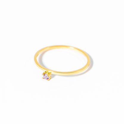 A minimalist gold ring with a single small square-cut light purple gemstone in a bezel setting, photographed on a clean white background.