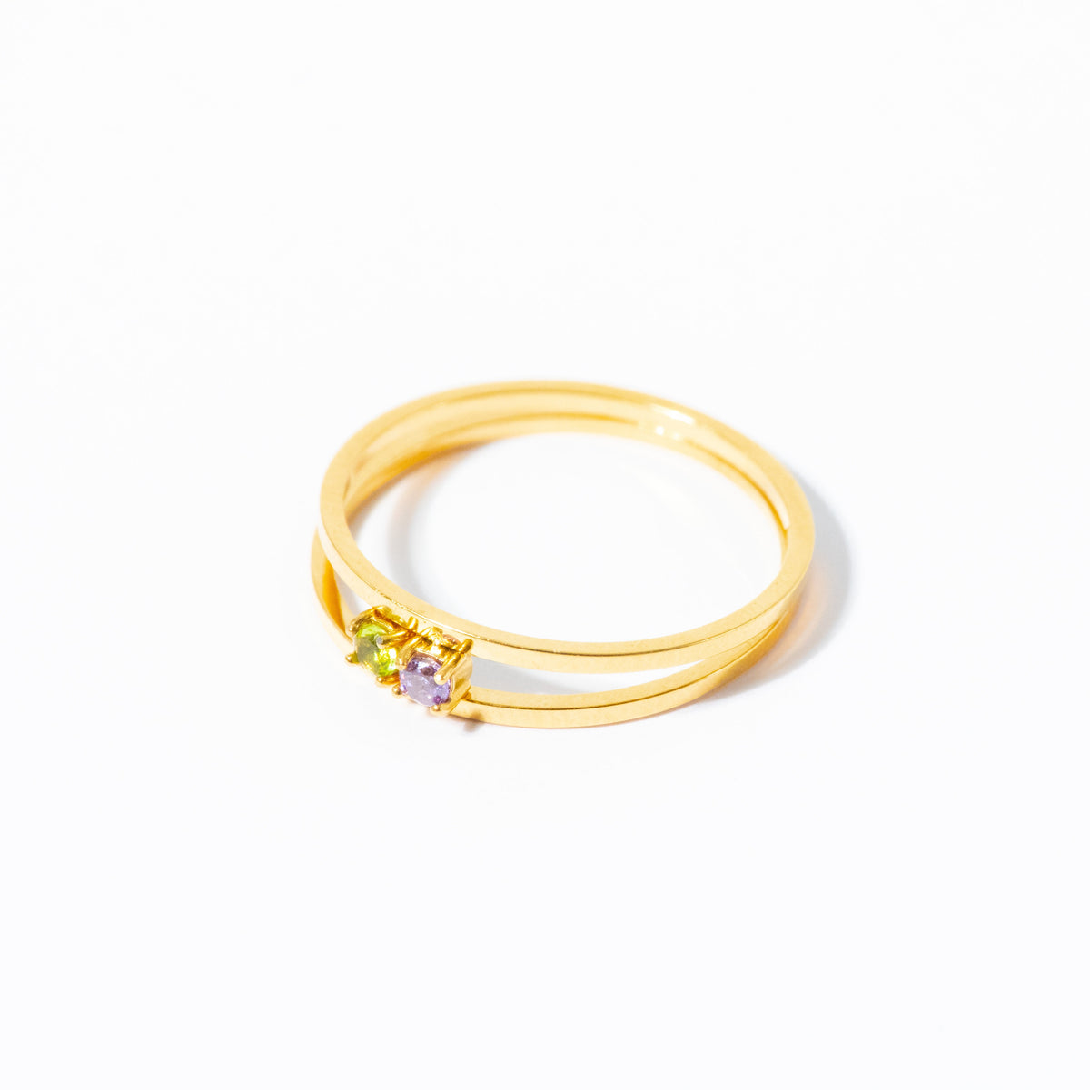 A gold double-band ring with a small cluster of green, purple, and clear gemstones on the front, set against a plain white background.