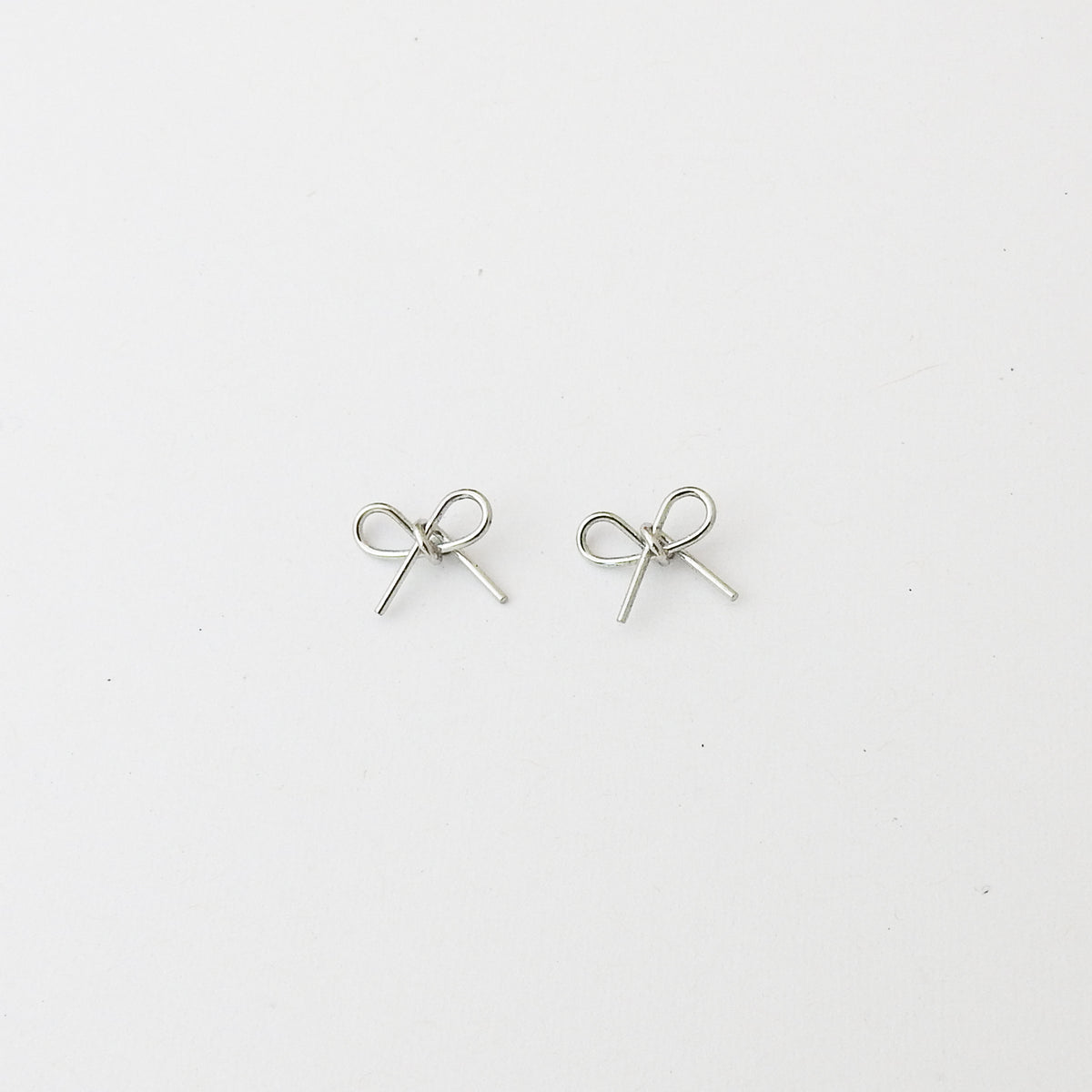 A pair of small silver bow-shaped stud earrings on a plain white background.