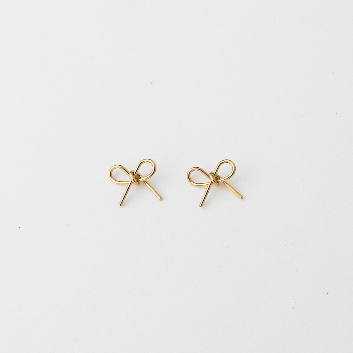 A pair of small gold bow-shaped stud earrings on a plain white background.