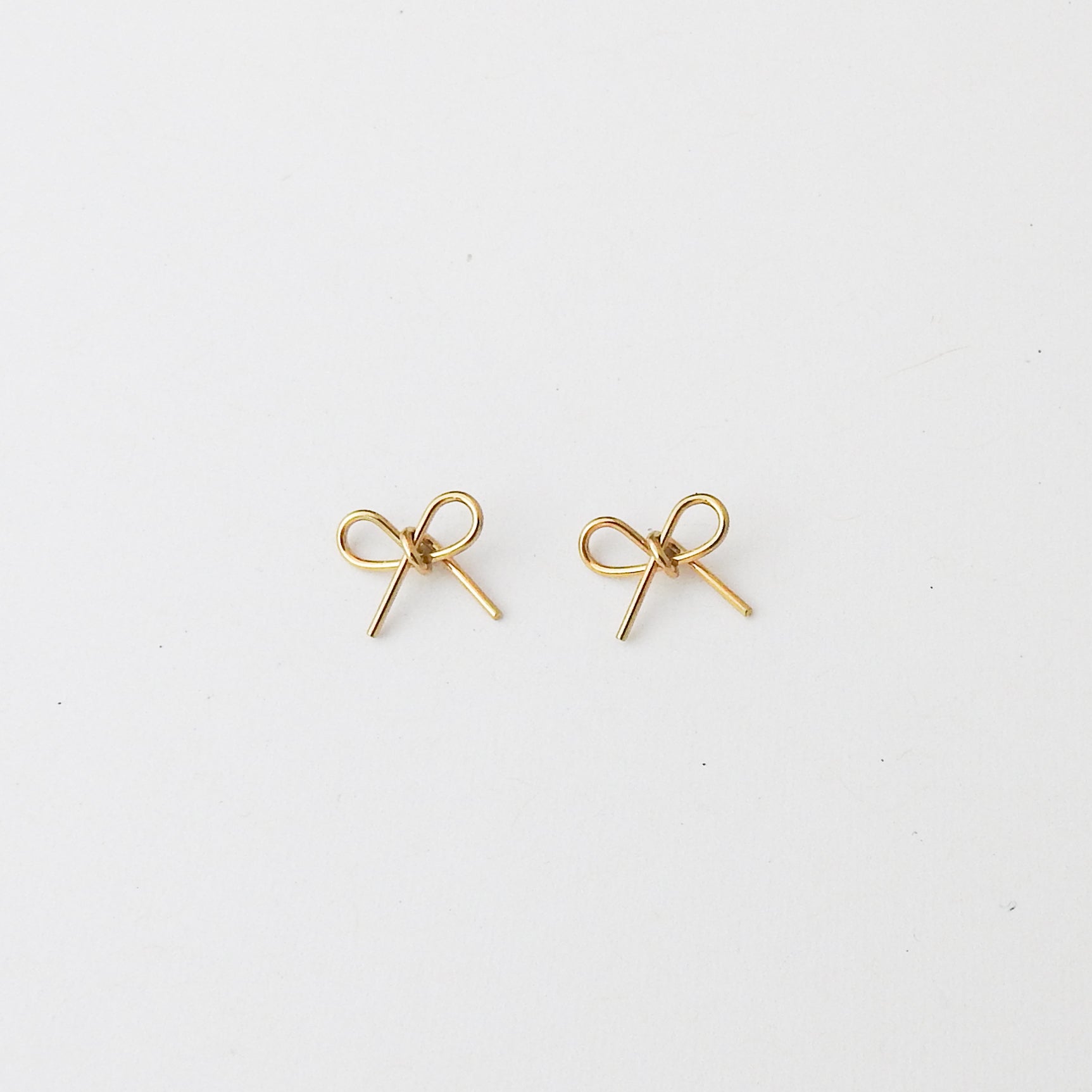 A pair of small gold bow-shaped stud earrings on a plain white background.