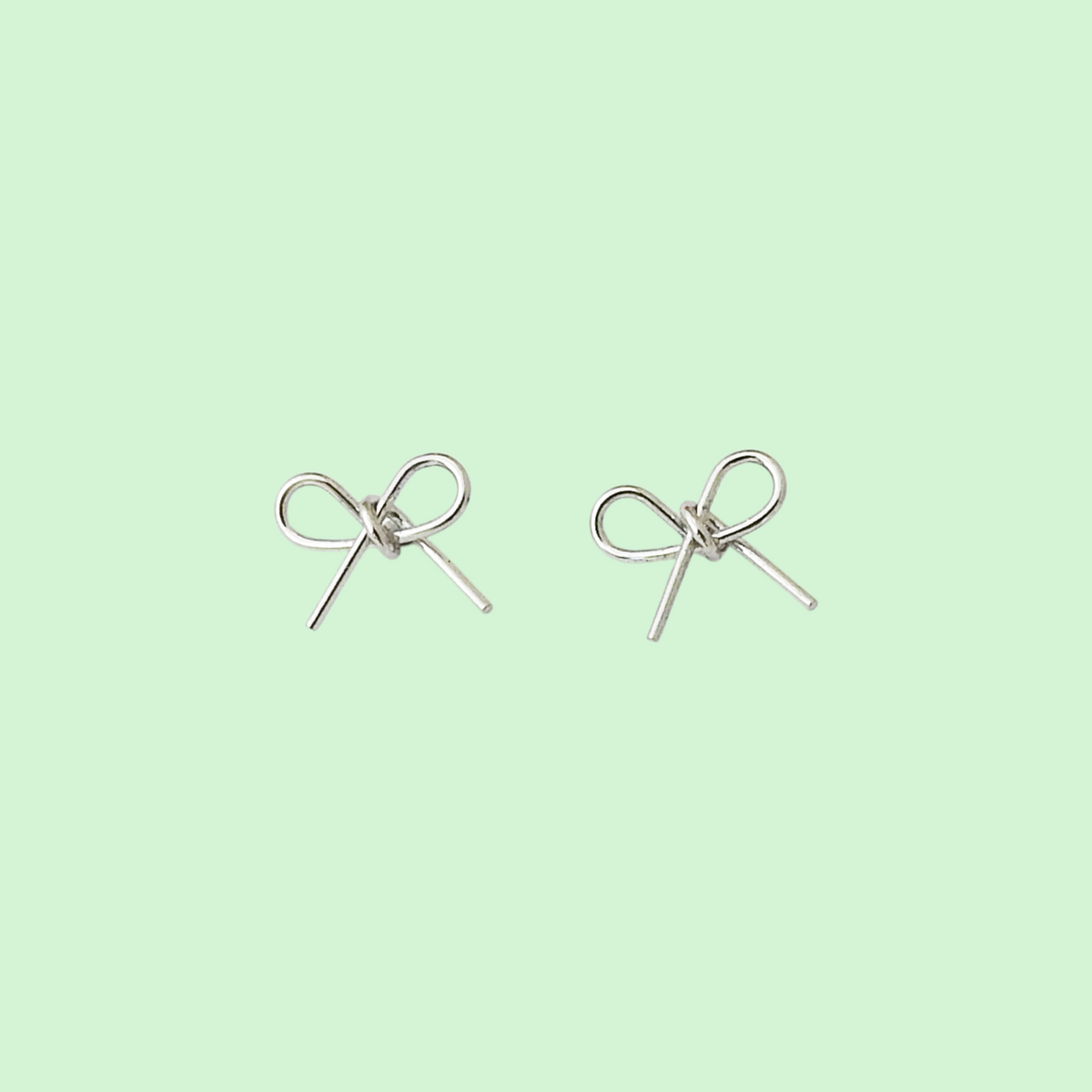 A pair of silver bow stud earrings on a solid pale mint green background.