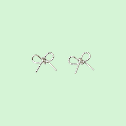 A pair of silver bow stud earrings on a solid pale mint green background.