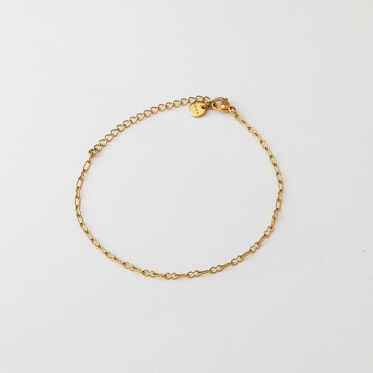 A delicate gold chain bracelet with a small round engraved charm, displayed on a clean white background.