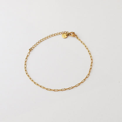 A delicate gold chain bracelet with a small round engraved charm, displayed on a clean white background.