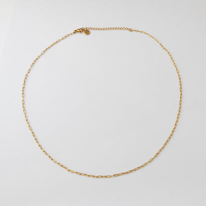 A delicate gold chain necklace with a small oval charm, arranged in a circle on a plain white background.
