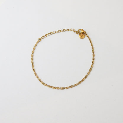 A delicate gold chain bracelet with a small lobster clasp and a round gold tag, displayed on a clean white background.
