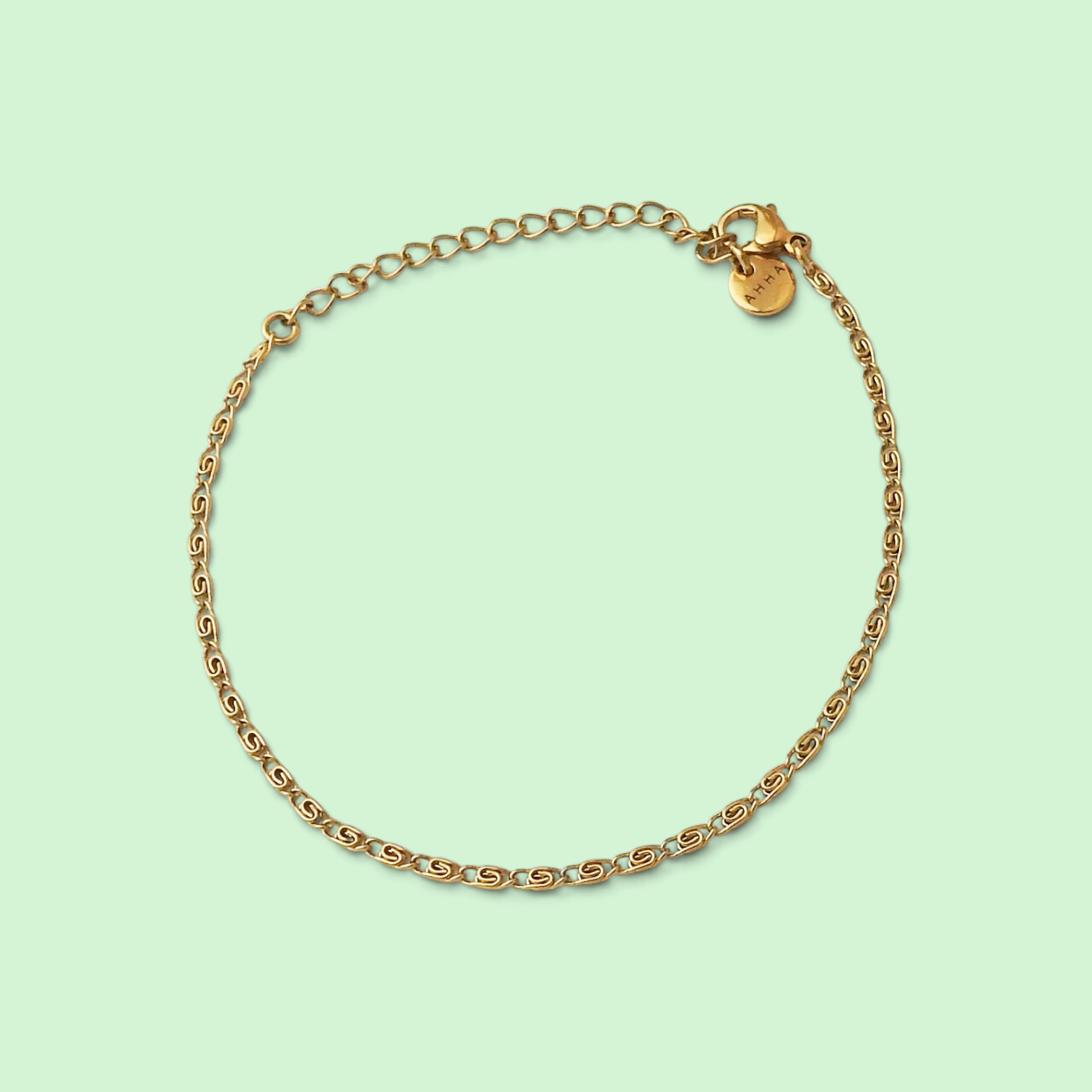A delicate gold chain bracelet with a lobster clasp and an adjustable extender link, displayed on a solid pale mint green background.
