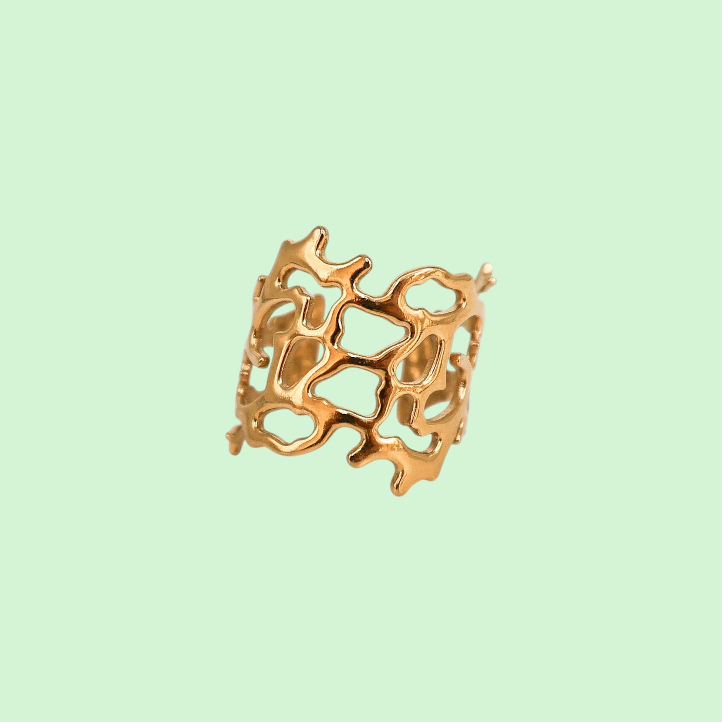 Gold ring with intricate coral design on a light green background