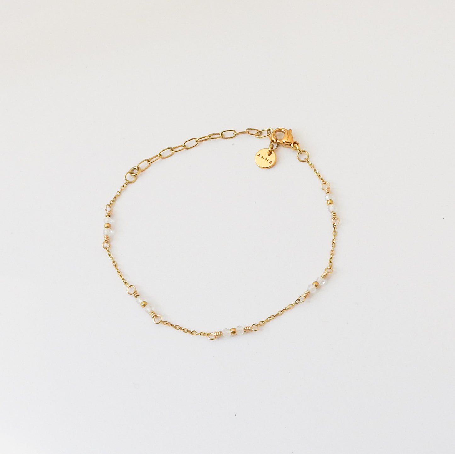 A delicate gold chain bracelet with small bead accents and a small engraved charm, displayed on a clean white background.