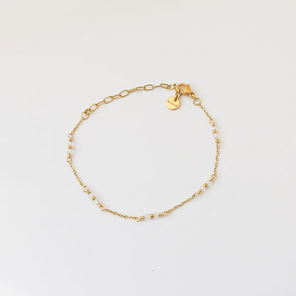 A delicate gold chain bracelet with small bead accents and a small engraved charm, displayed on a clean white background.