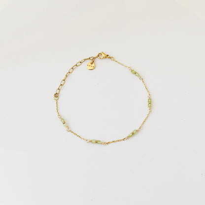 A delicate gold chain bracelet with small light green beads and a small heart-shaped charm, displayed on a clean white background.