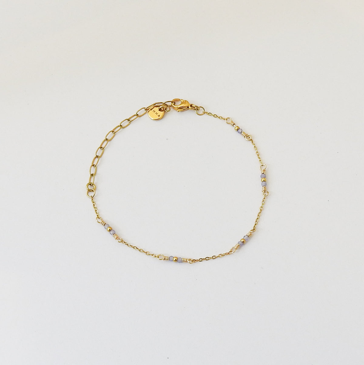 A delicate gold chain bracelet with small light blue faceted beads spaced along the band, displayed on a clean white background.