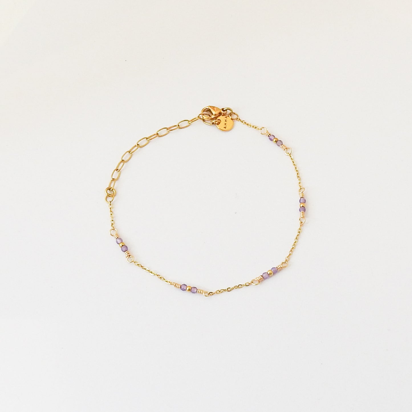 A delicate gold chain bracelet with small purple and clear beads spaced along the front, displayed on a clean white background.