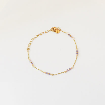 A delicate gold chain bracelet with small purple and clear beads spaced along the front, displayed on a clean white background.
