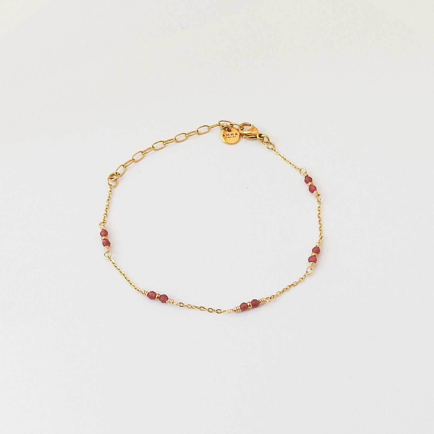 A delicate gold chain bracelet with small red beads spaced along the chain, displayed on a clean white background.