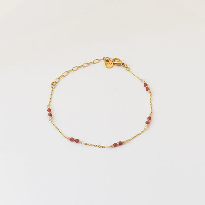 A delicate gold chain bracelet with small red beads spaced along the chain, displayed on a clean white background.